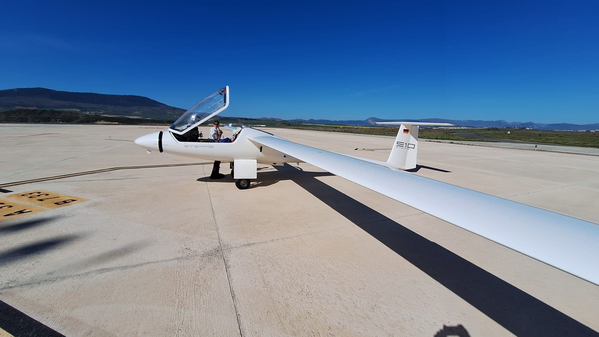 Stemme S10 mit ausgebreiteten Tragflächen auf dem Vorfeld, Berge im Hintergrund